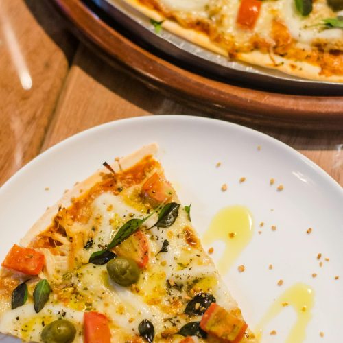 Close-up of a delicious pizza slice with toppings like cheese, olives, and tomatoes on a white plate.